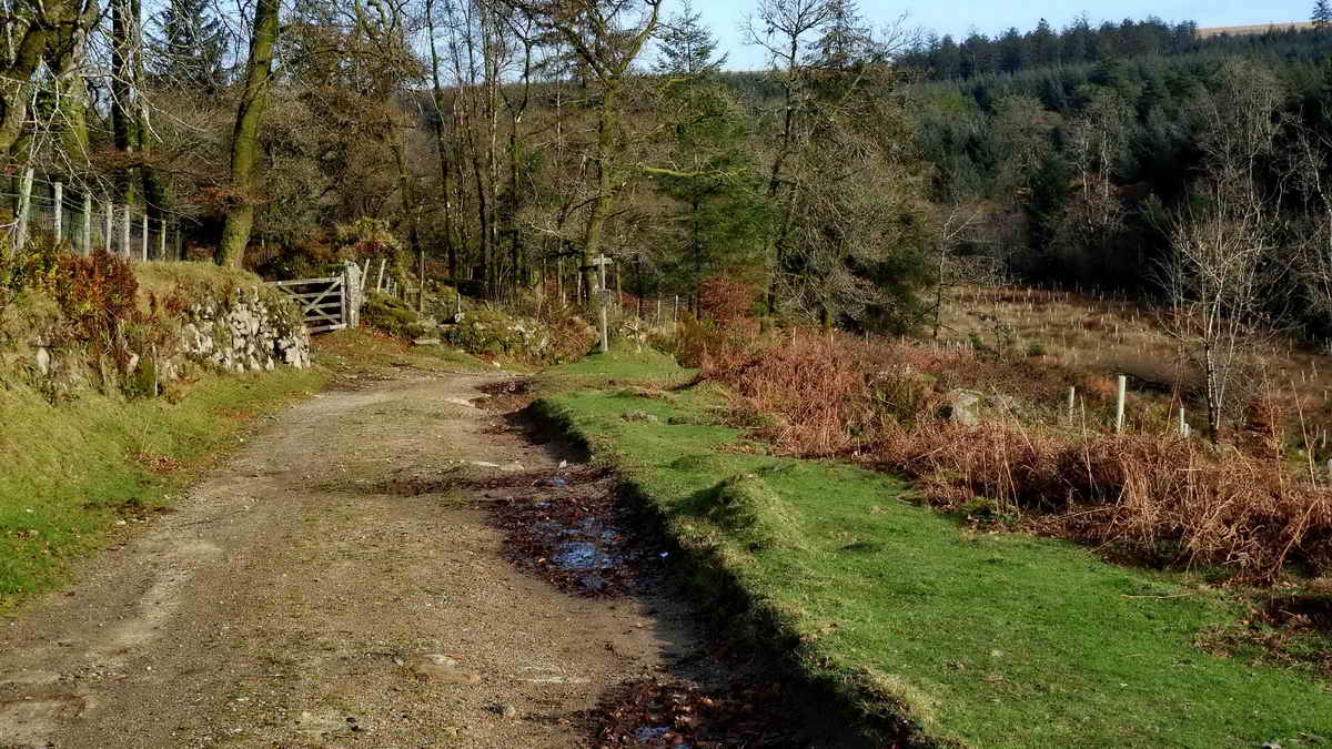 Approaching Leathertor Farm, gate and stile on the left. The signpost is seen next below, and down the slope on the right is the fougou